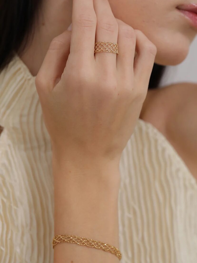 Close-up of a woman's hand displaying a golden ring and bracelet, with her face partially visible in the background.