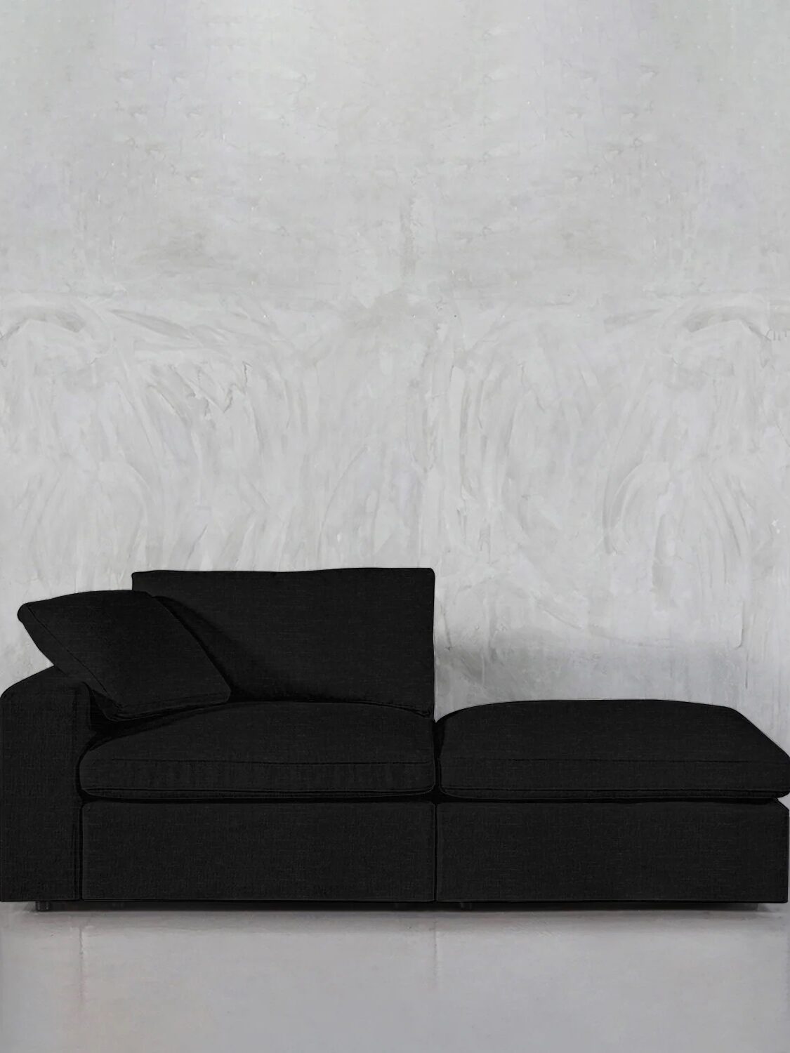 A black sectional sofa with a chaise lounge is situated against a plain, light-colored wall.