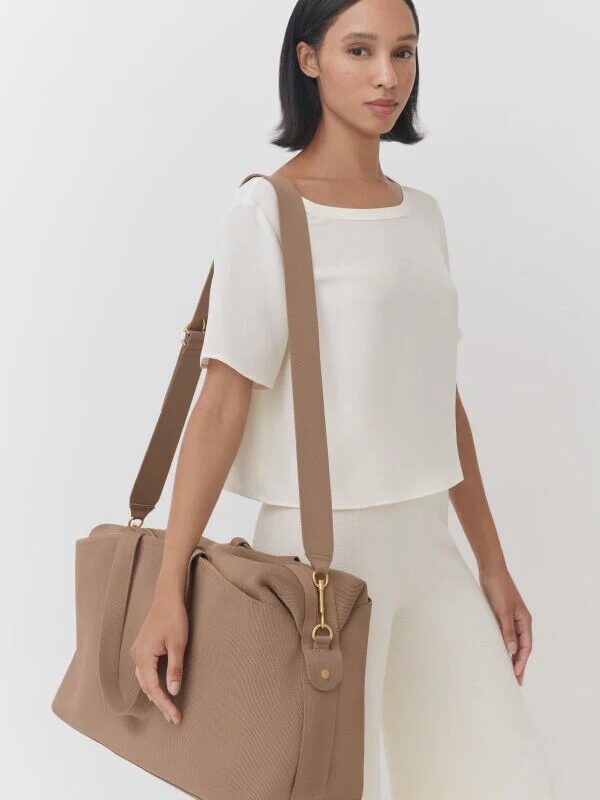 A model carries a Cuyana travel bag in beige on their shoulder.