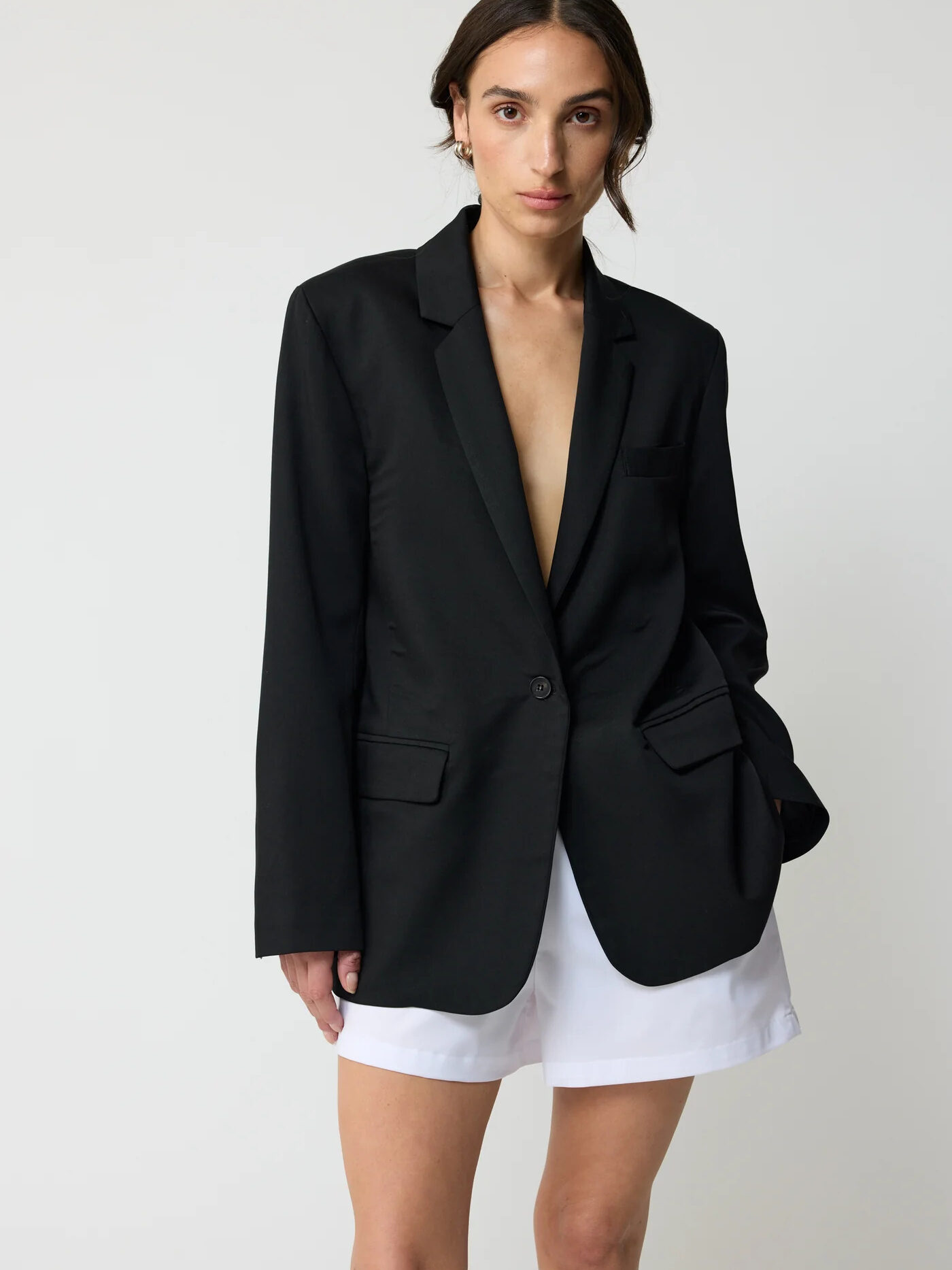 A woman wearing a black blazer over a white dress, posing against a light background.