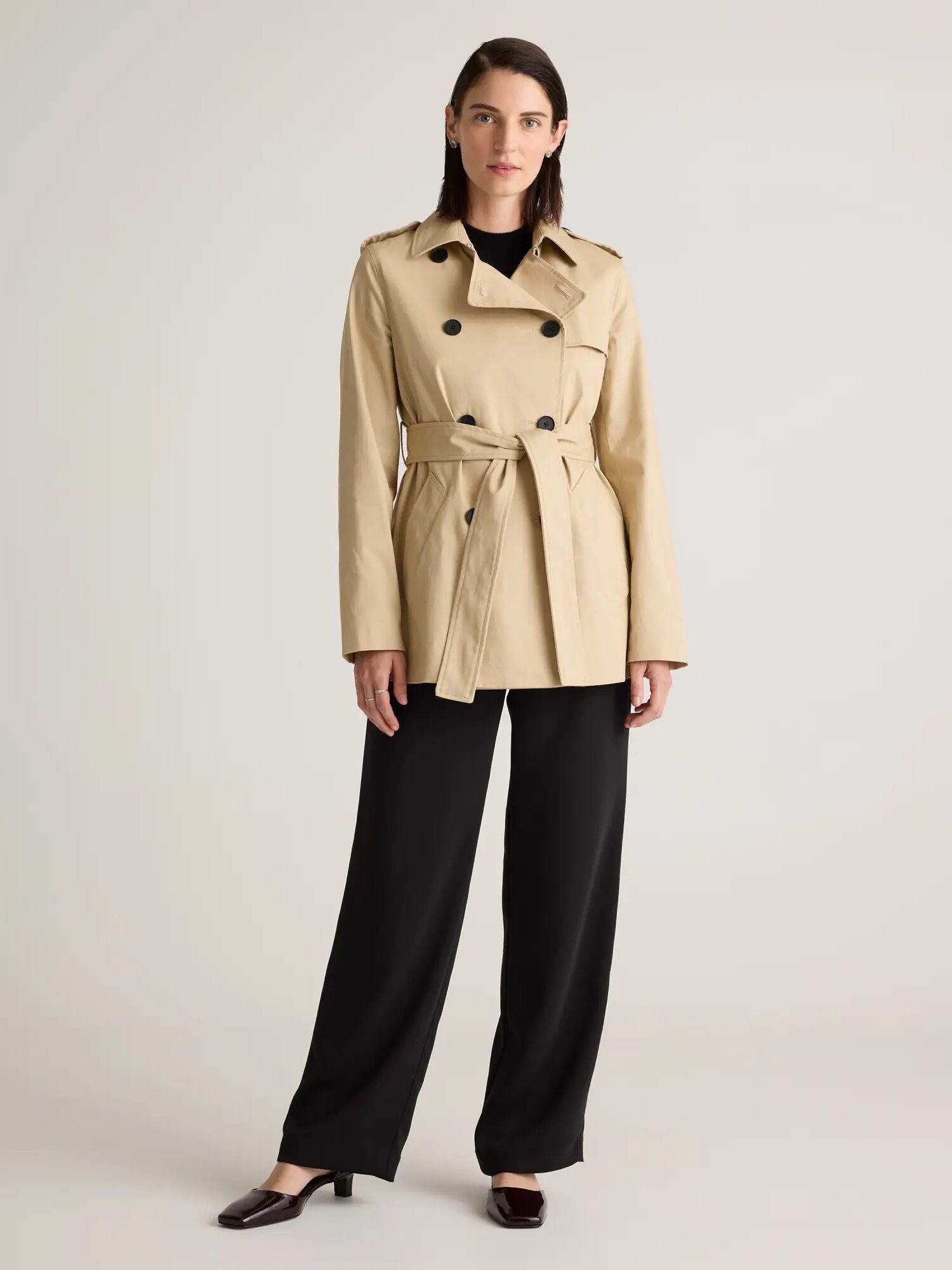 A model wearing a khaki short trench coat from Quince. 