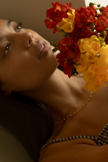 A woman looking toward a cluster of red and yellow freesia flowers.