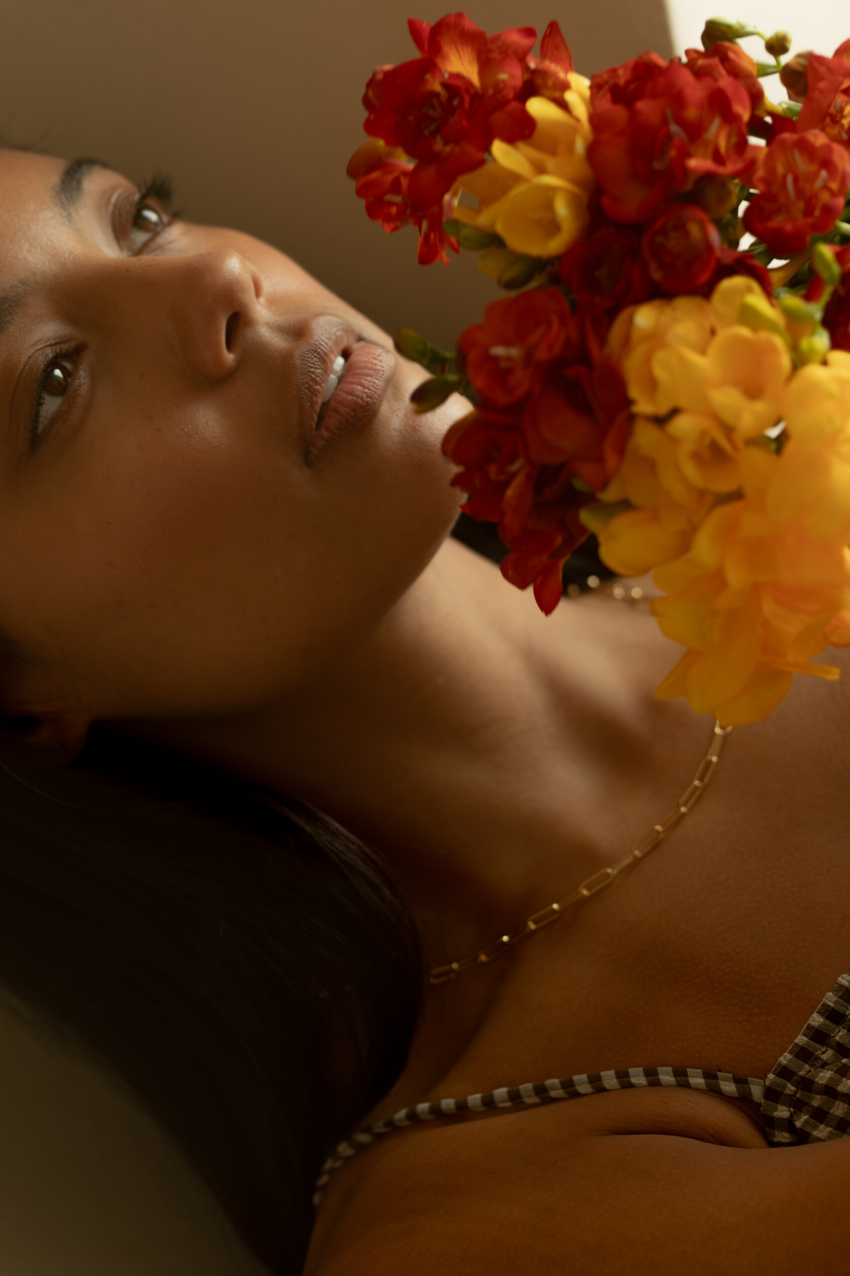 A woman looking toward a cluster of red and yellow freesia flowers.