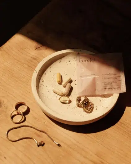 A small dish holds several pills and a pair of gold earrings. Next to the dish is a gold necklace and a packet labeled "Perel" with an outline of what's inside.