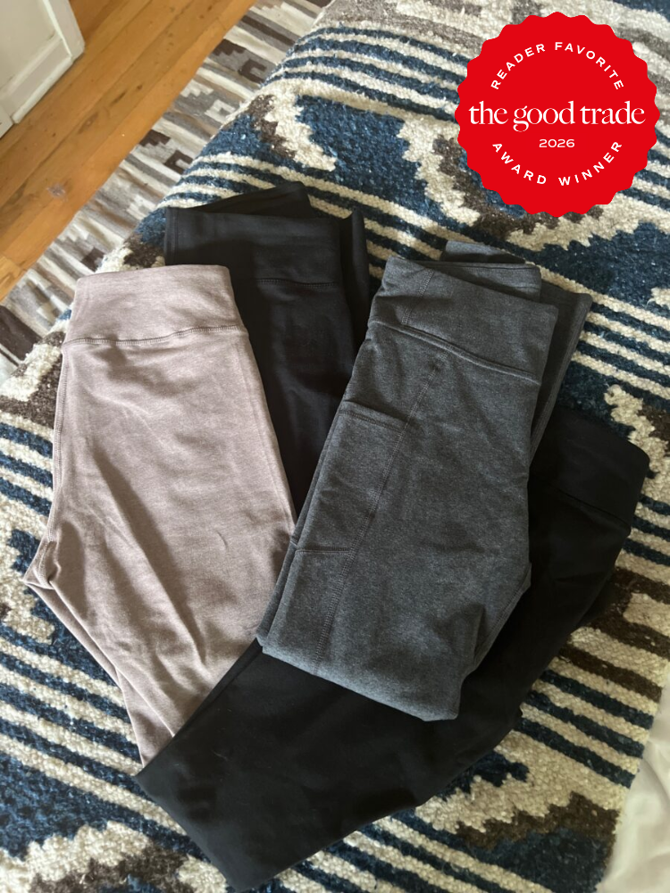 Four pairs of folded leggings in gray, taupe, and black are laid out on a patterned bedspread. A "The Good Trade 2026 Award Winner" badge appears in the corner.