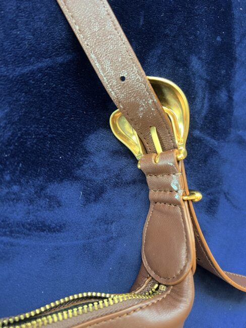 Close-up of a brown leather bag strap with gold hardware against a dark blue fabric background, reminiscent of details highlighted in many a Cuyana review.