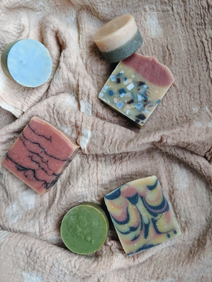 Five handmade artisan soaps, each with unique colors and patterns, are arranged on a textured beige fabric.