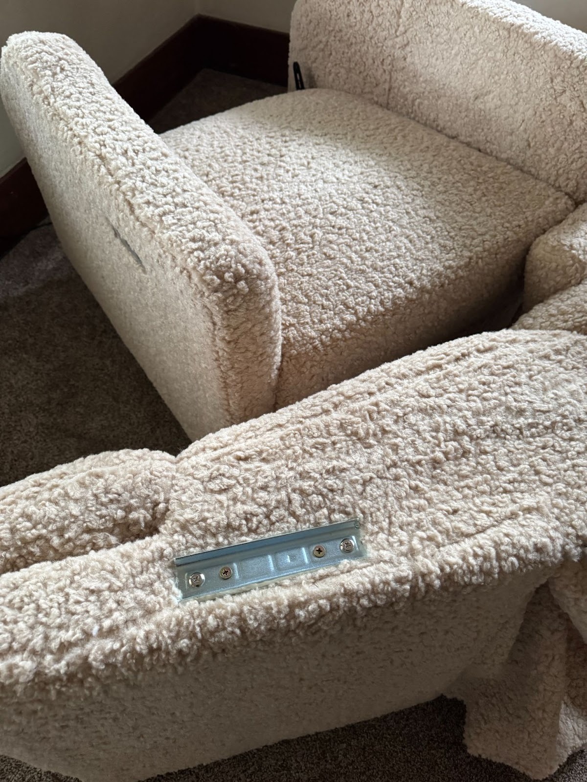 Two sections of a beige, textured upholstered sofa are positioned next to each other on carpet, with a visible metal connecting bracket on one piece.
