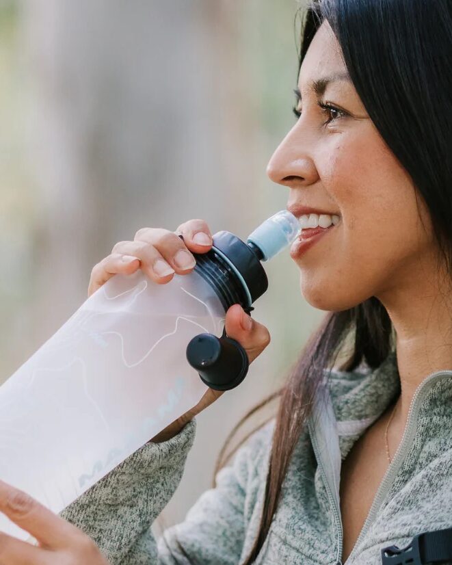 Woman outdoors drinking from a translucent water bottle with a black cap and flip lid; "Lightweight Water Bottle" text above.