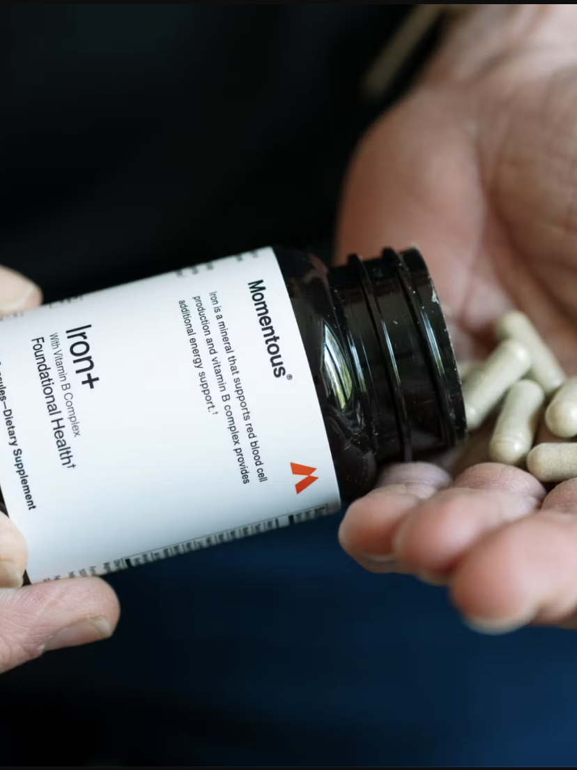 A person pours several Iron+ supplement capsules from a Momentous bottle into their hand.
