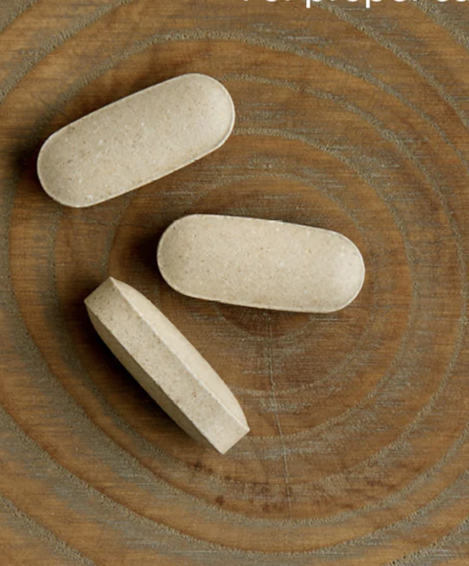 Three beige, oval-shaped tablets are placed on a wooden surface with circular grain patterns.
