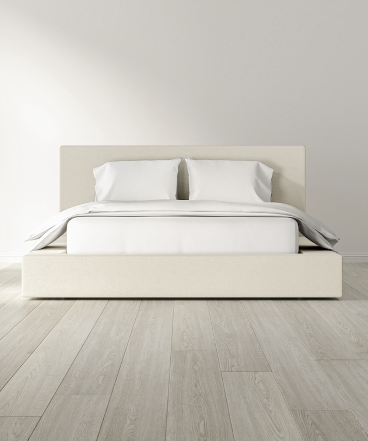 A minimalist bedroom features a beige upholstered bed with white bedding and two pillows, set on light wood flooring against a plain light-colored wall.