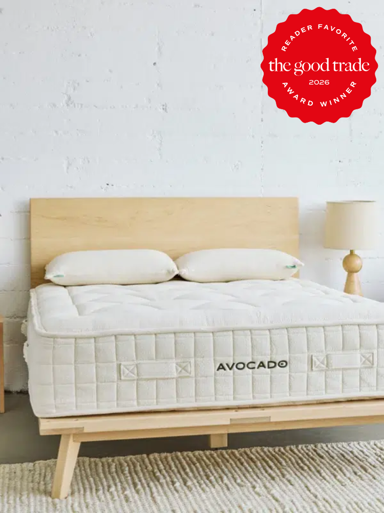 A modern wooden bed frame with an Avocado mattress and two pillows in a minimalist bedroom; a red award badge is displayed in the upper right corner.