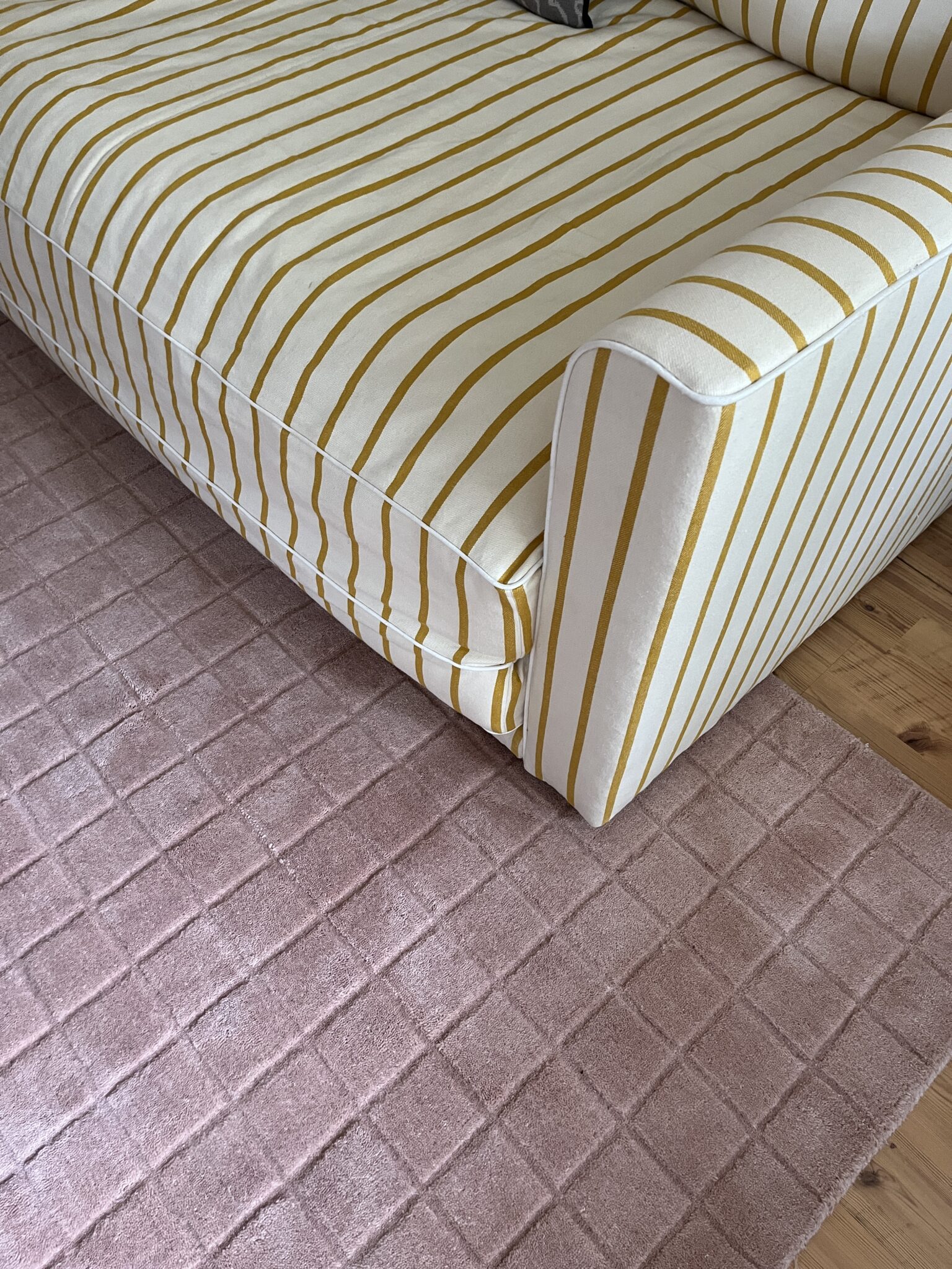 A yellow and white striped sofa is positioned next to a light pink checkered rug on a wooden floor.