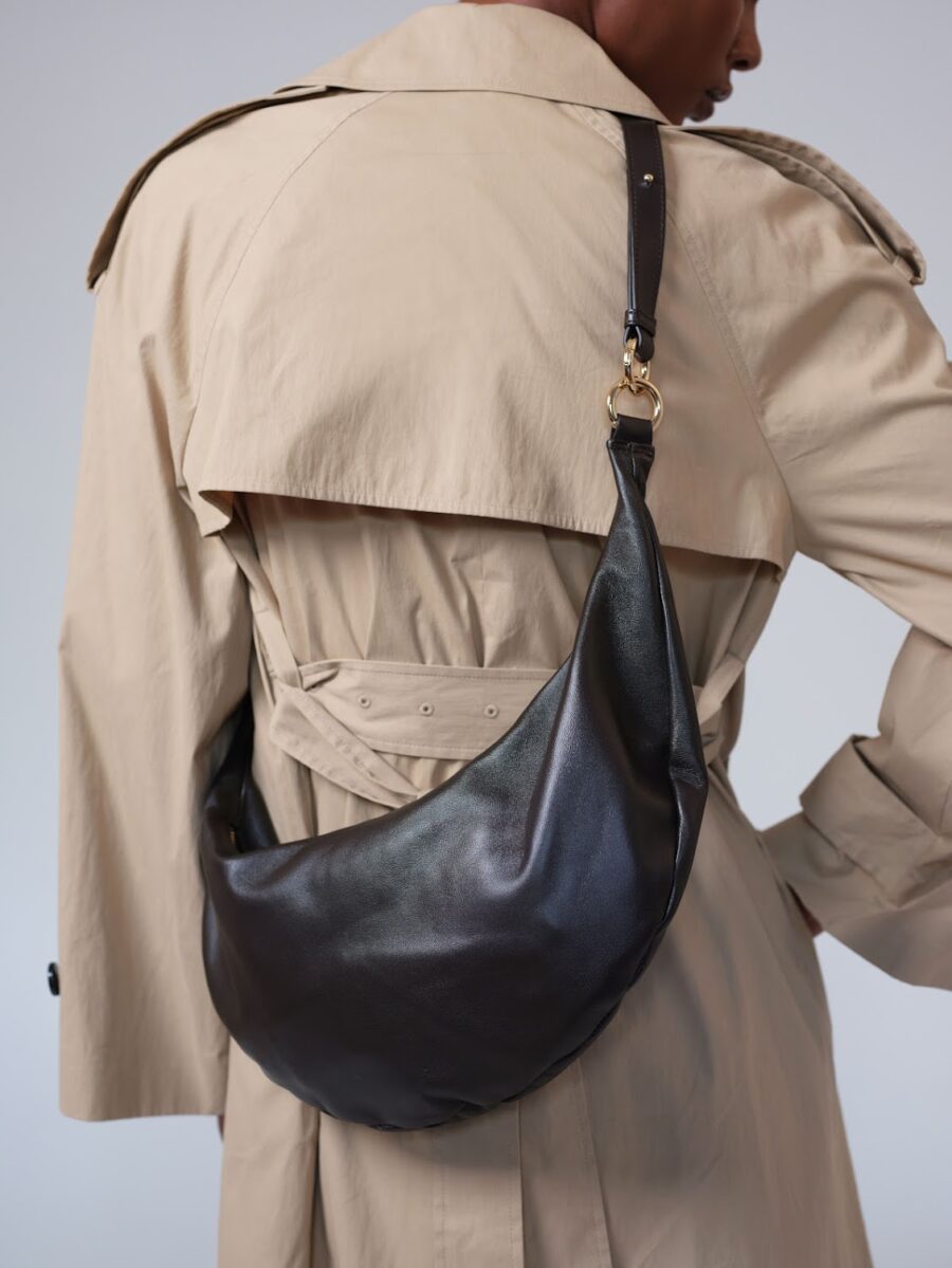 Person wearing a beige trench coat with a large black leather shoulder bag slung across their back.
