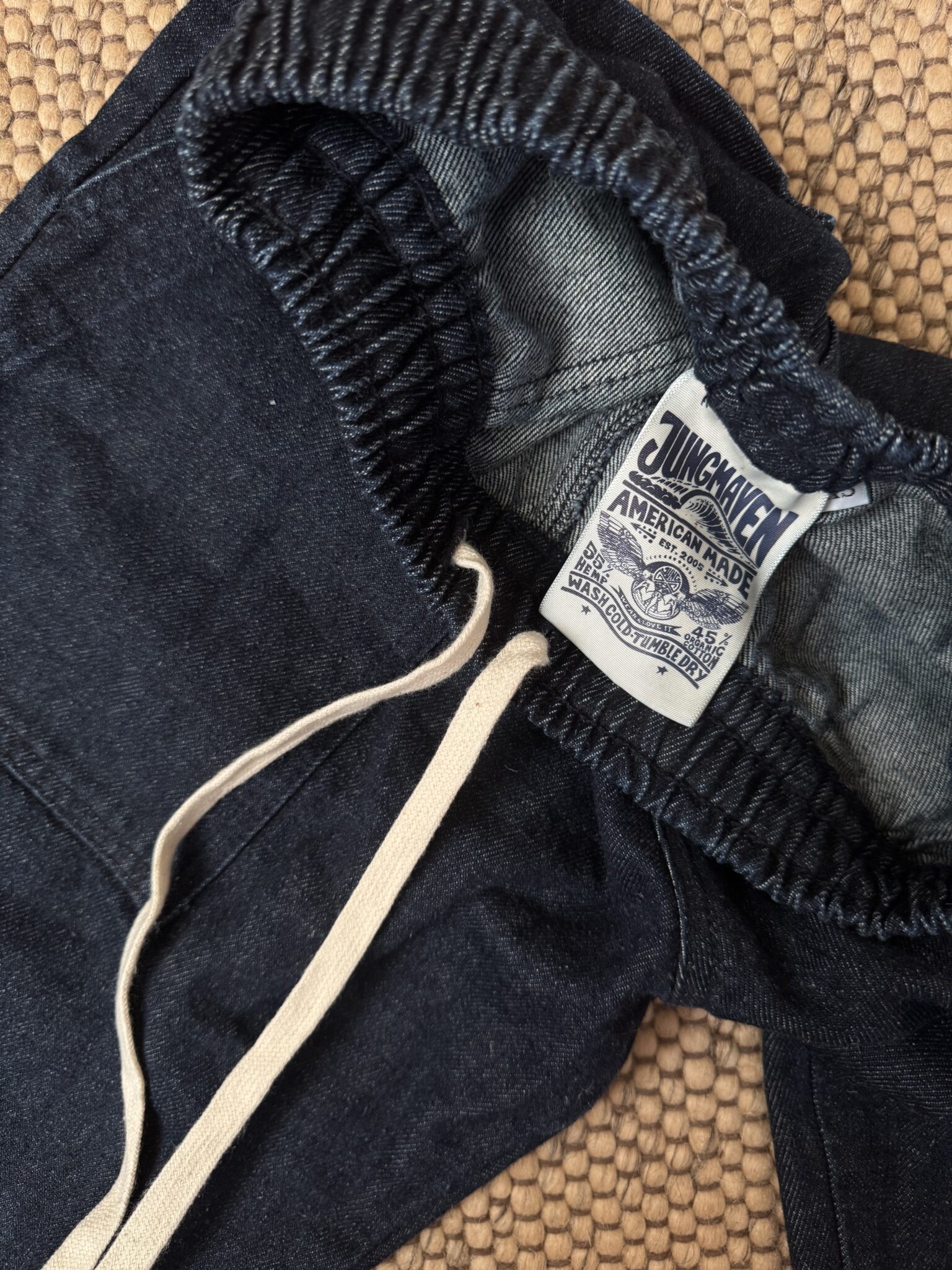 Close-up of dark blue elastic-waist pants with white drawstring, showing an inside label that reads "Jungmaven American Made.