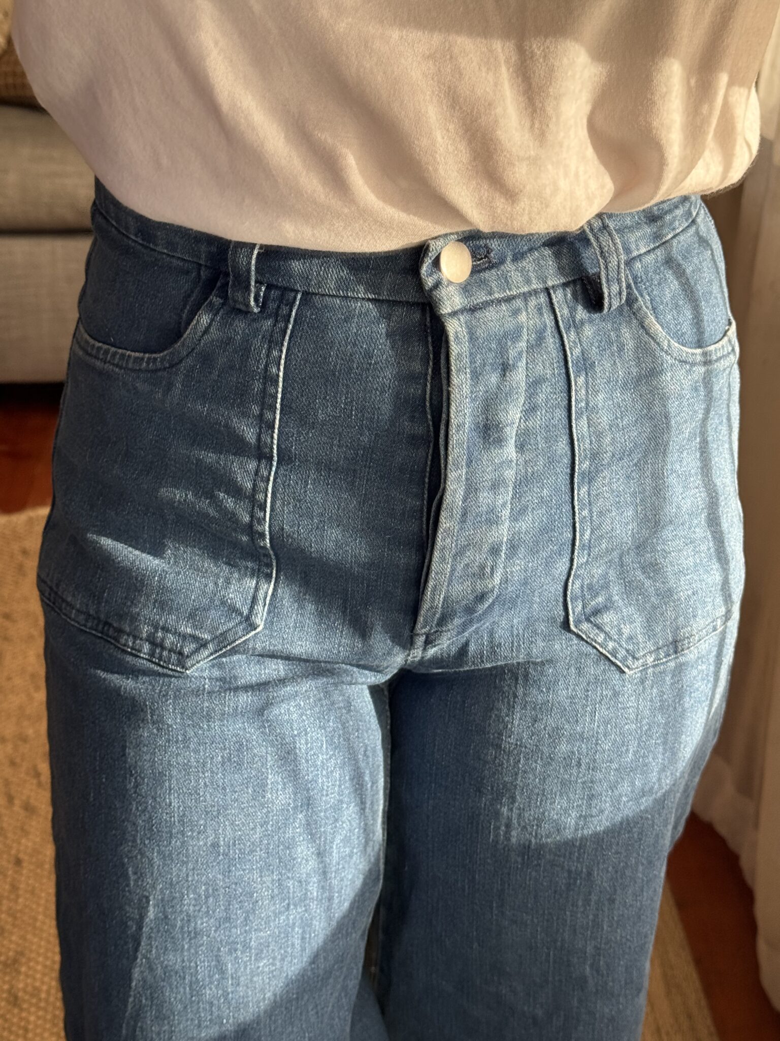 Person wearing high-waisted blue jeans and a white shirt, standing indoors in natural sunlight.