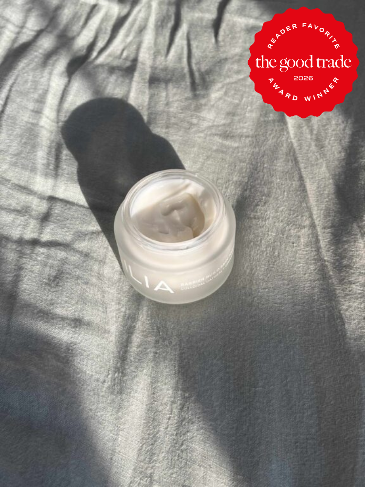An open jar of ILIA face cream sits on a light gray fabric in sunlight. A red badge in the corner reads "The Good Trade 2026 Reader Favorite Award Winner.