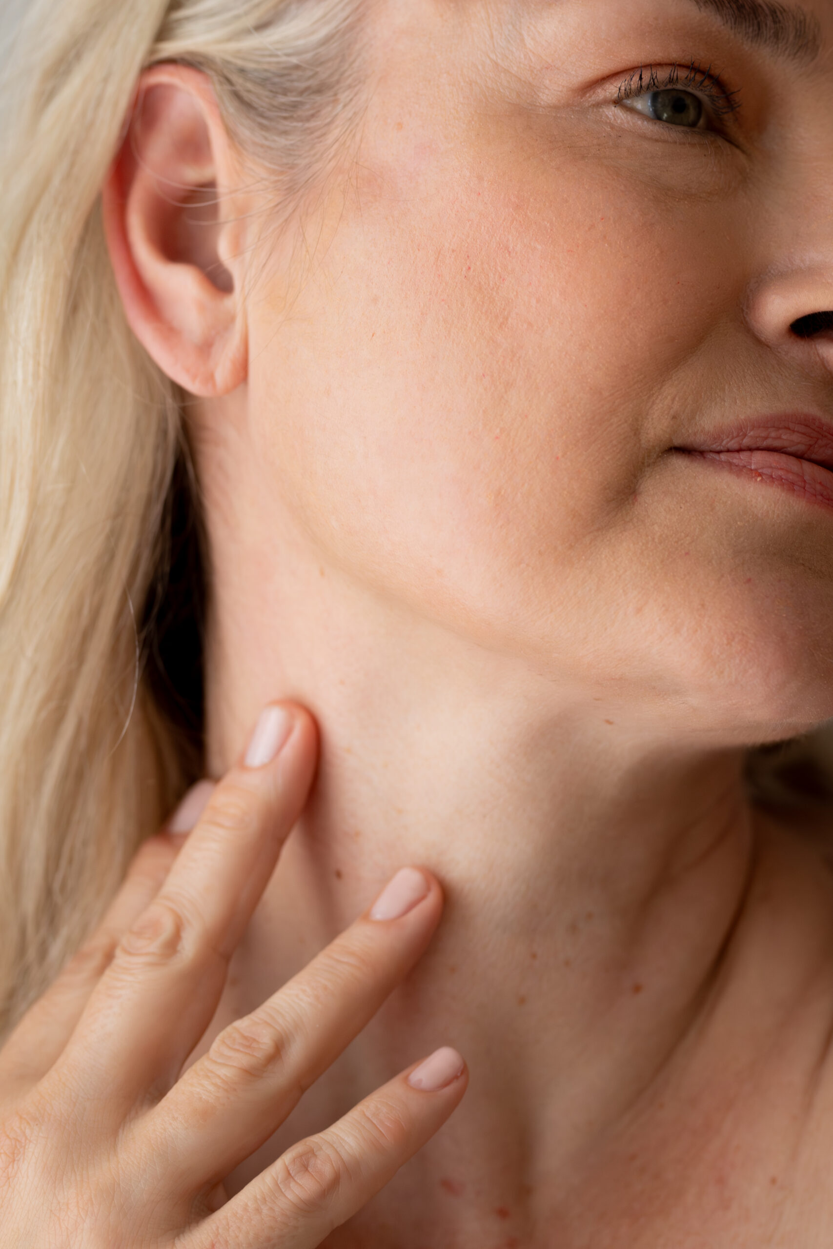A close-up profile view of a woman touching her neck with her hand.