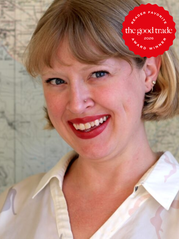 A woman with short blonde hair and red lipstick smiles in front of a map. A "The Good Trade 2026 Reader Favorite Award Winner" badge appears in the top right corner.