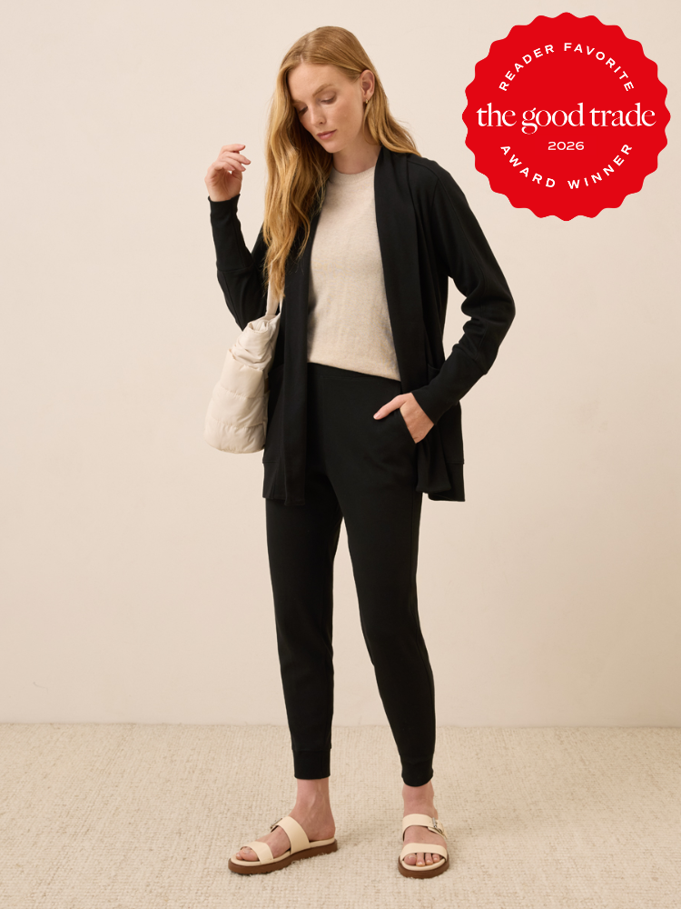 A woman stands wearing a beige top, black cardigan, and matching black joggers with white sandals and a cream shoulder bag. "The Good Trade 2026 Reader Favorite Award Winner" badge is displayed.