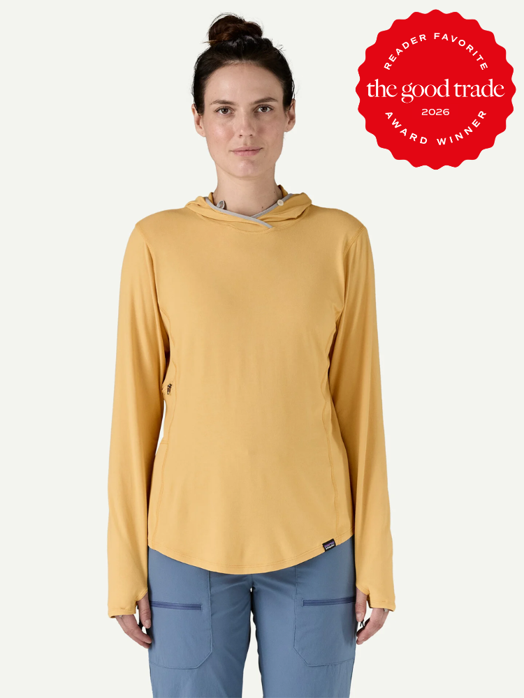 A woman wears a yellow long-sleeve hooded shirt and blue pants, standing against a plain background. A red "The Good Trade 2026 Reader Favorite Award Winner" badge appears in the corner.