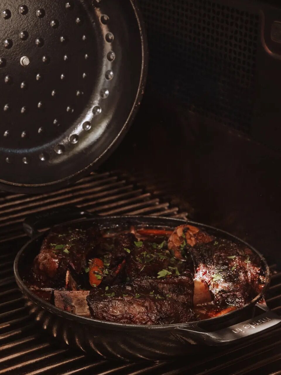 A pan of braised short ribs with vegetables is cooking inside an oven, with the lid partially open and steam visible.