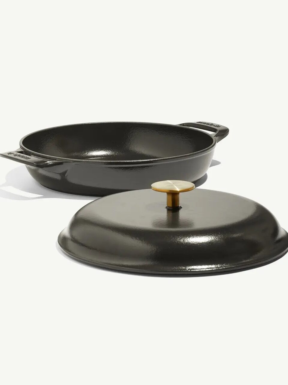 A round black cast iron pan with two side handles and a matching lid with a brass knob, both shown on a white background.