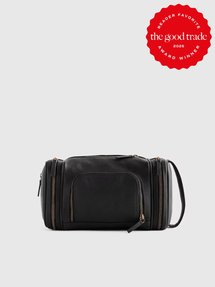 Black leather dopp kit with multiple zippered compartments, shown on a plain background. A red badge in the top right corner reads "The Good Trade Award Winner 2025".