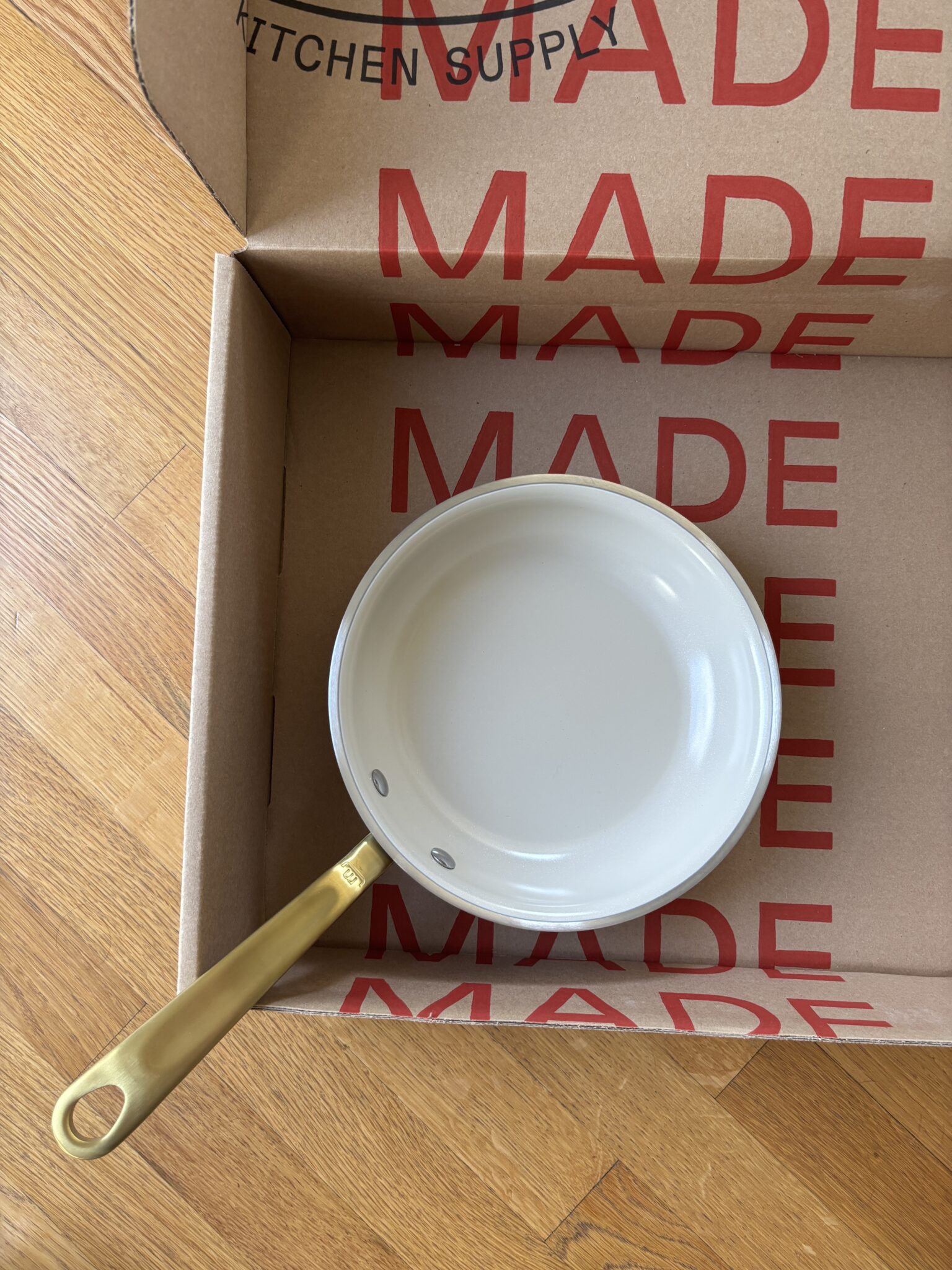 A small white saucepan with a gold handle sits inside an open cardboard box with "MADE" printed in large red letters.