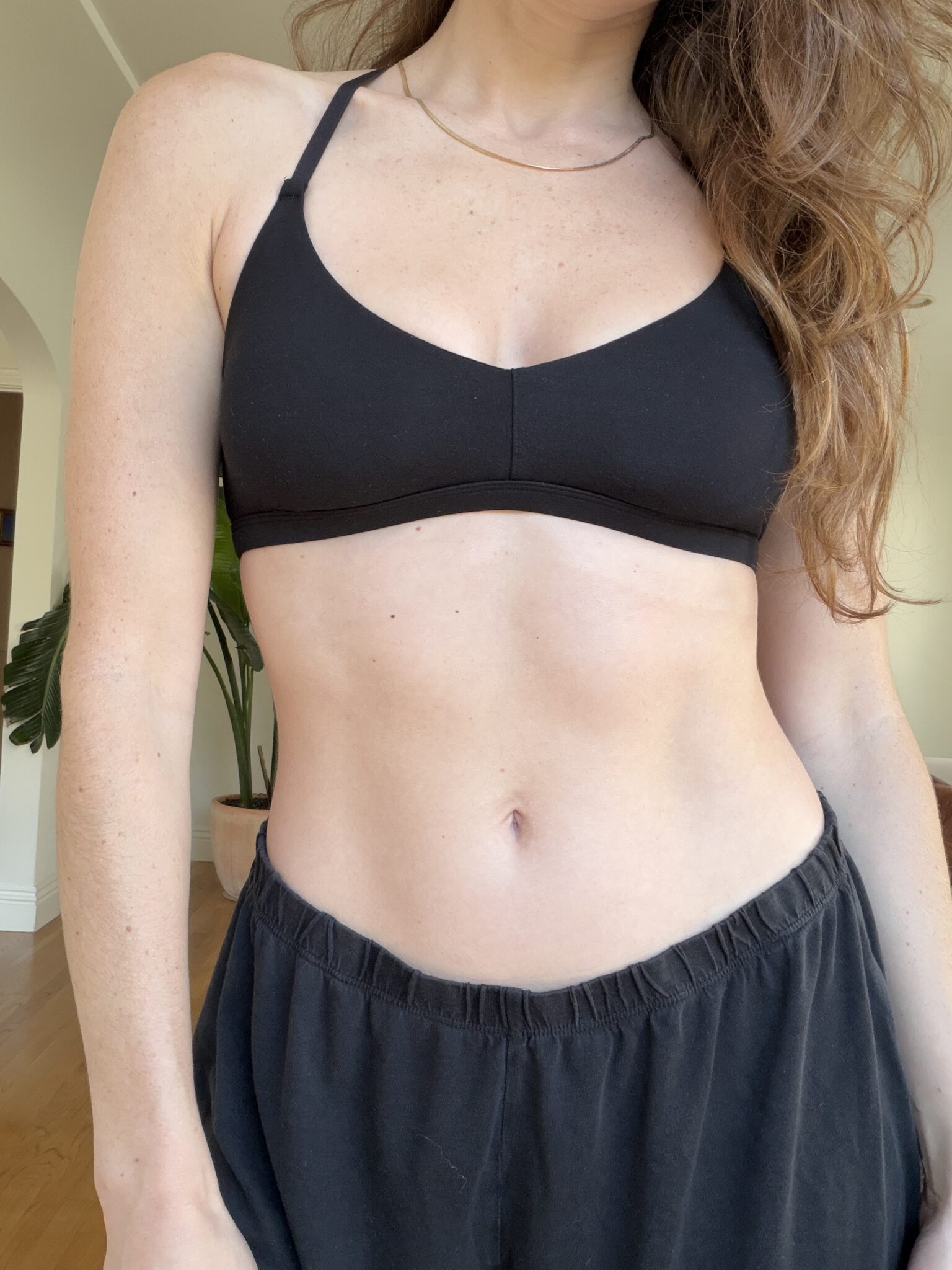 A woman wearing a black sports bra and black pants stands indoors with part of her face and hair visible.