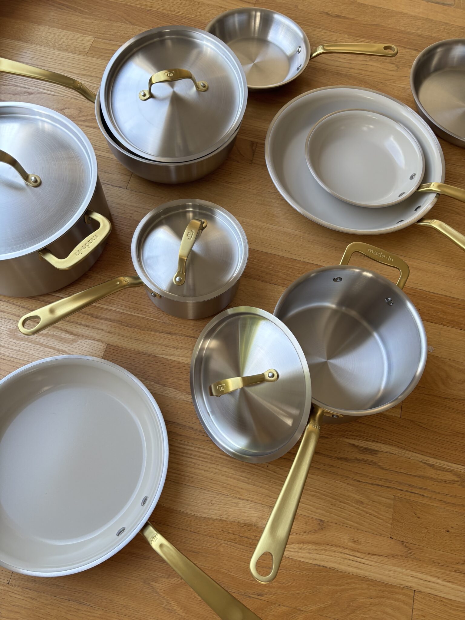 A set of stainless steel pots and pans with gold handles and lids arranged on a wooden floor.