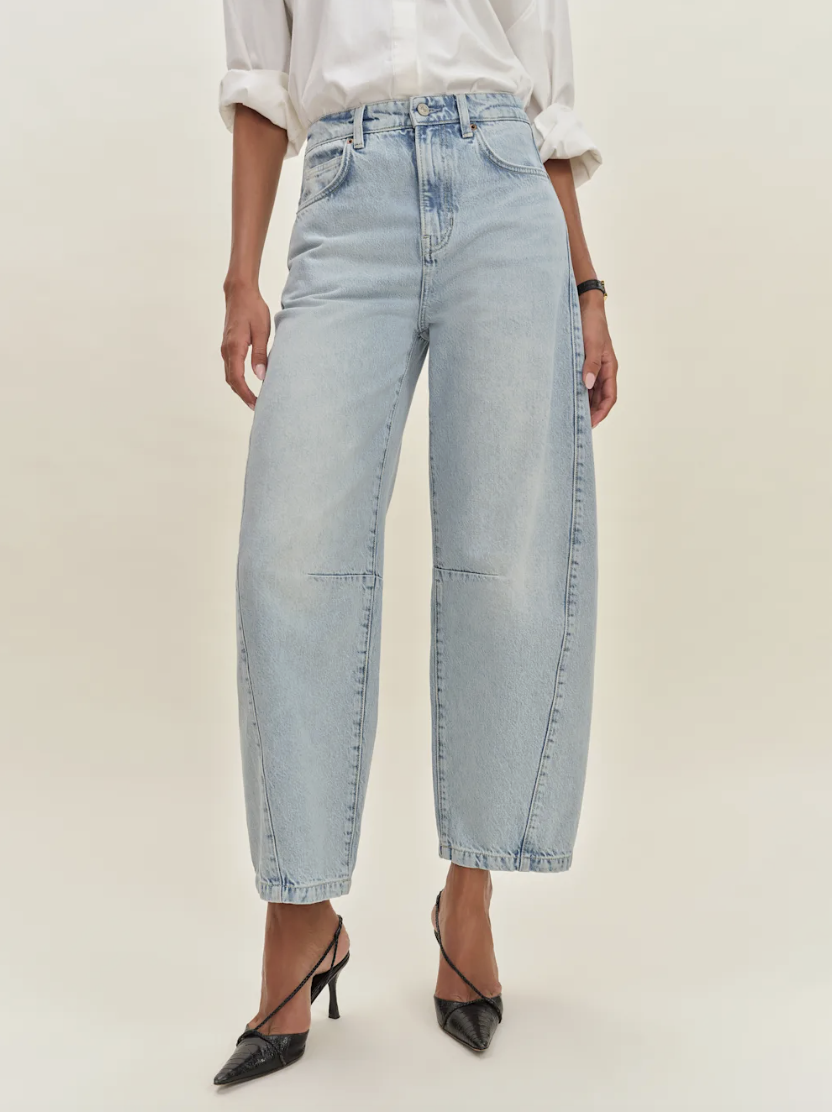 A person wearing light blue wide-leg jeans, a white long-sleeve shirt with rolled-up sleeves, and black pointed-toe heels.