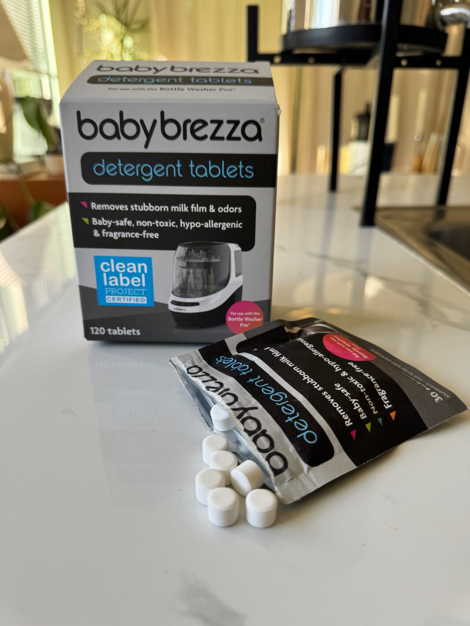 A box of Baby Brezza detergent tablets sits on a kitchen counter, with several white tablets spilled out of an opened packet in front of it.