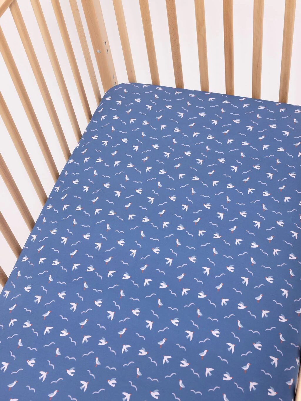 A wooden crib with a blue fitted sheet featuring a pattern of small white birds and pink accents.