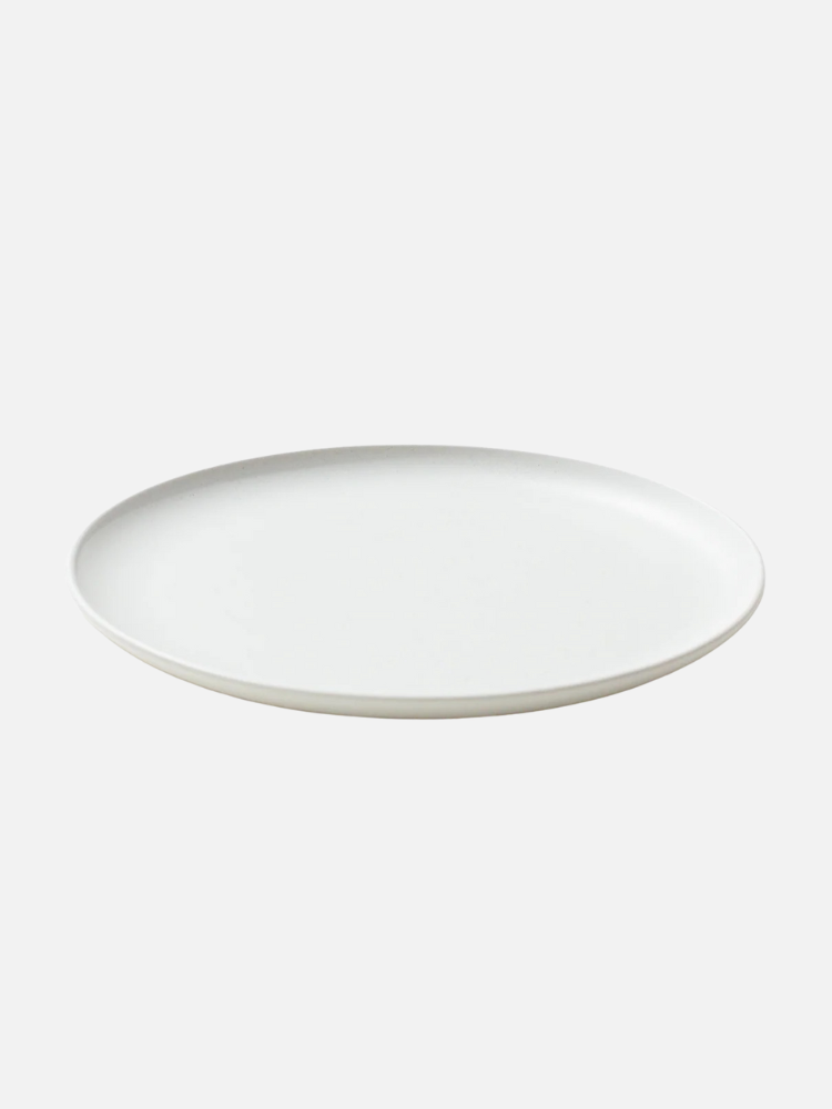A plain, round, white ceramic plate on a light gray background.