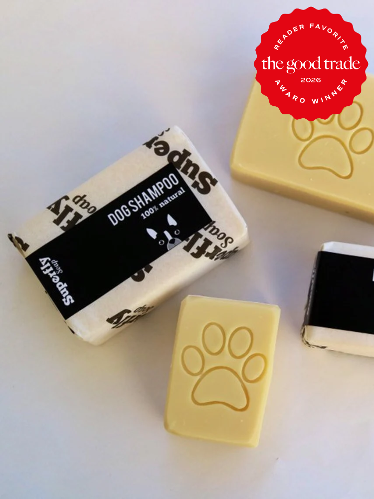 Three bars of dog shampoo, one wrapped and labeled “Dog Shampoo 100% natural,” two unwrapped with paw print imprints. A red “The Good Trade Award Winner 2026” badge is in the corner.
