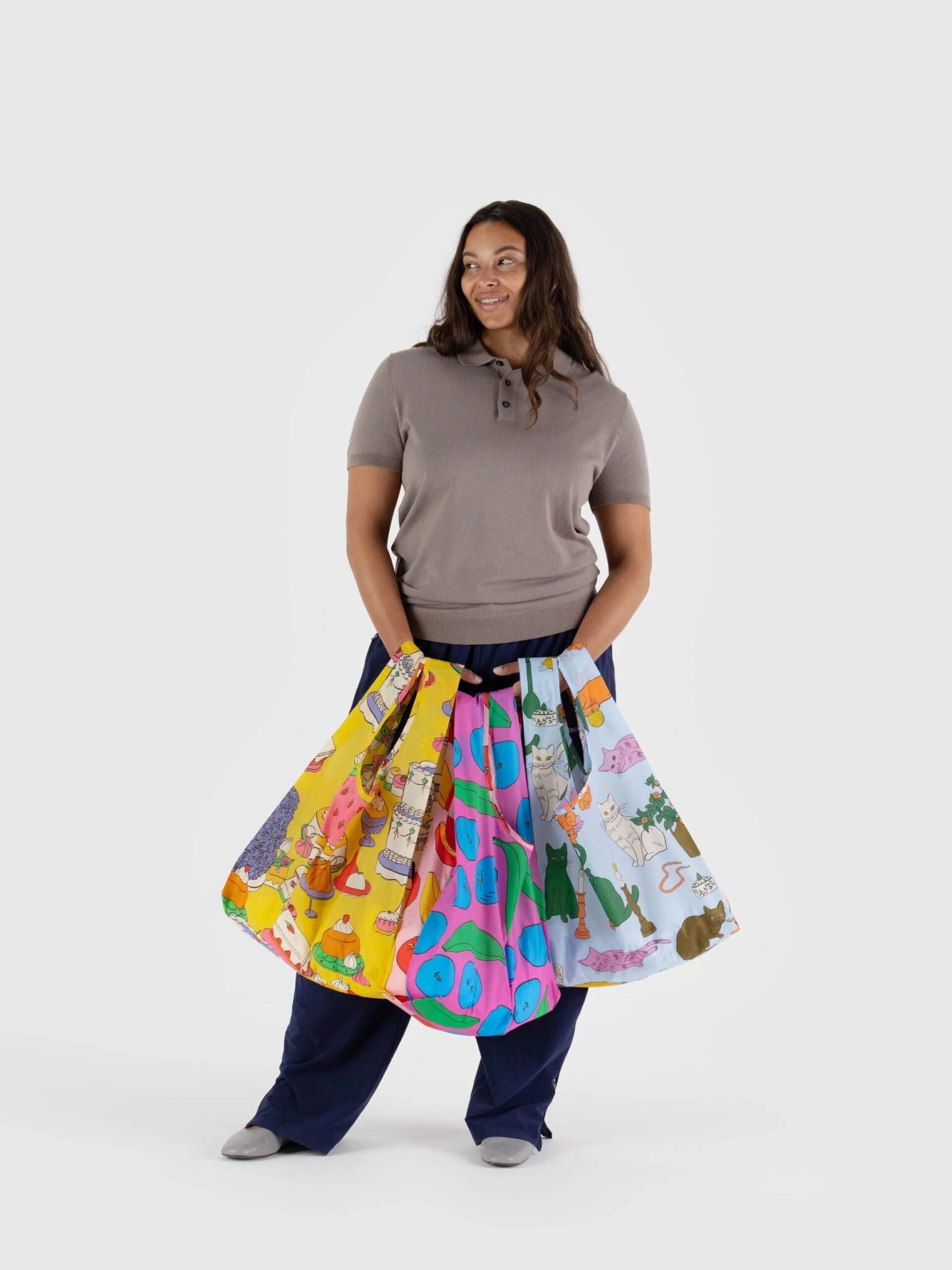 A woman stands holding four colorful, patterned tote bags, each featuring different playful designs, against a plain white background.