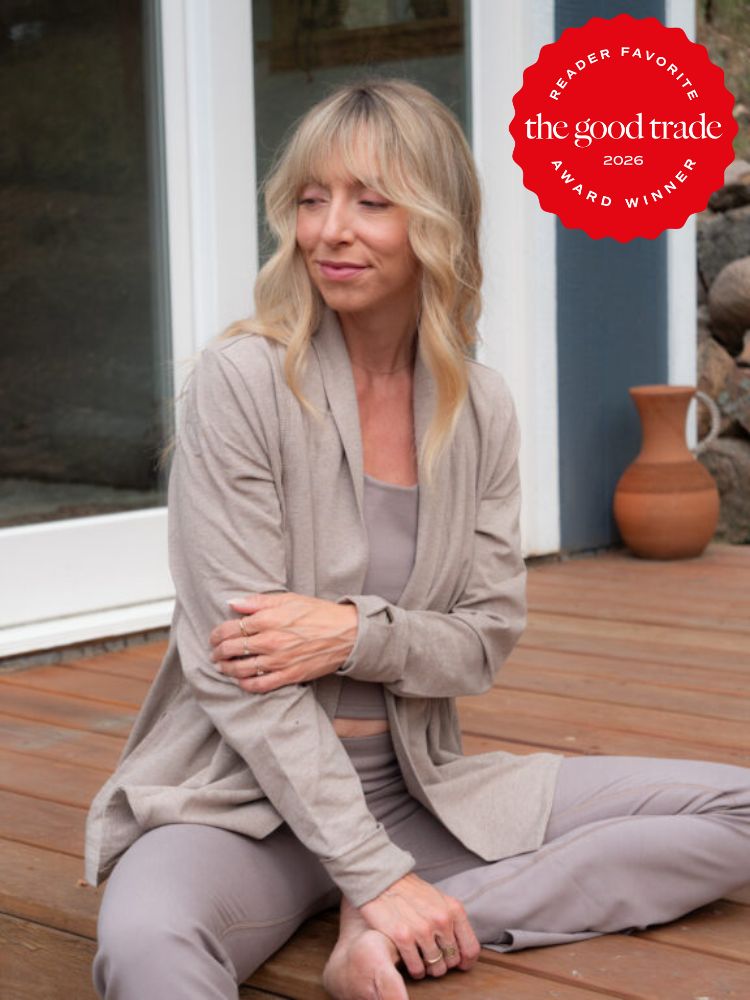 A woman in neutral loungewear sits on a wooden deck outside, with a clay pitcher in the background. A "The Good Trade 2026 Award Winner" badge is in the top right corner.