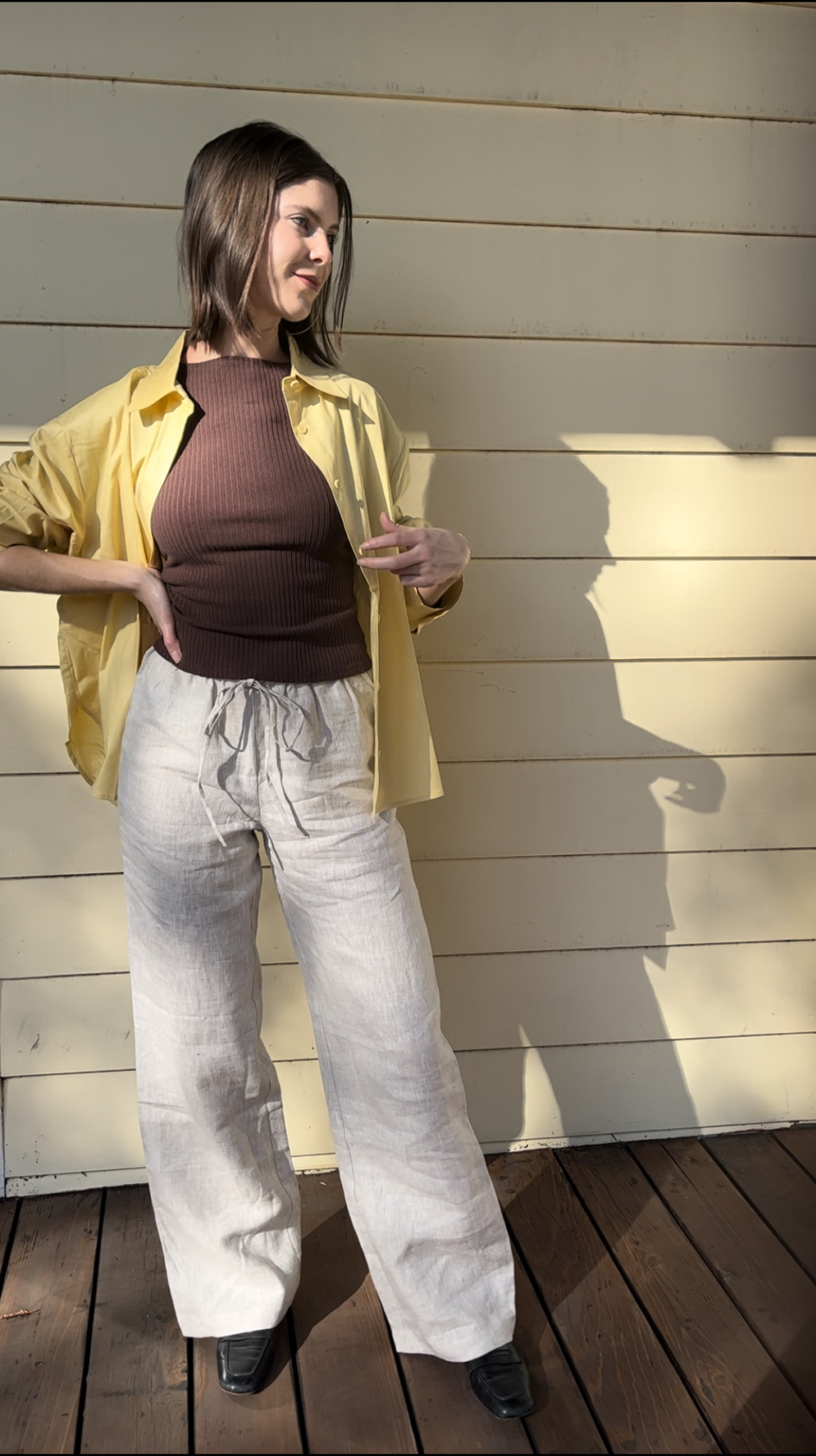 A woman standing outside wearing a yellow shirt and white pants.