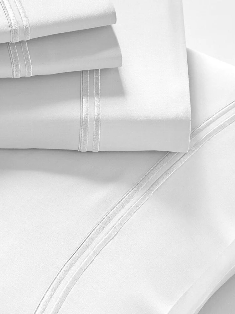 Neatly folded white bed sheets with double-stitched detailing on a light surface.