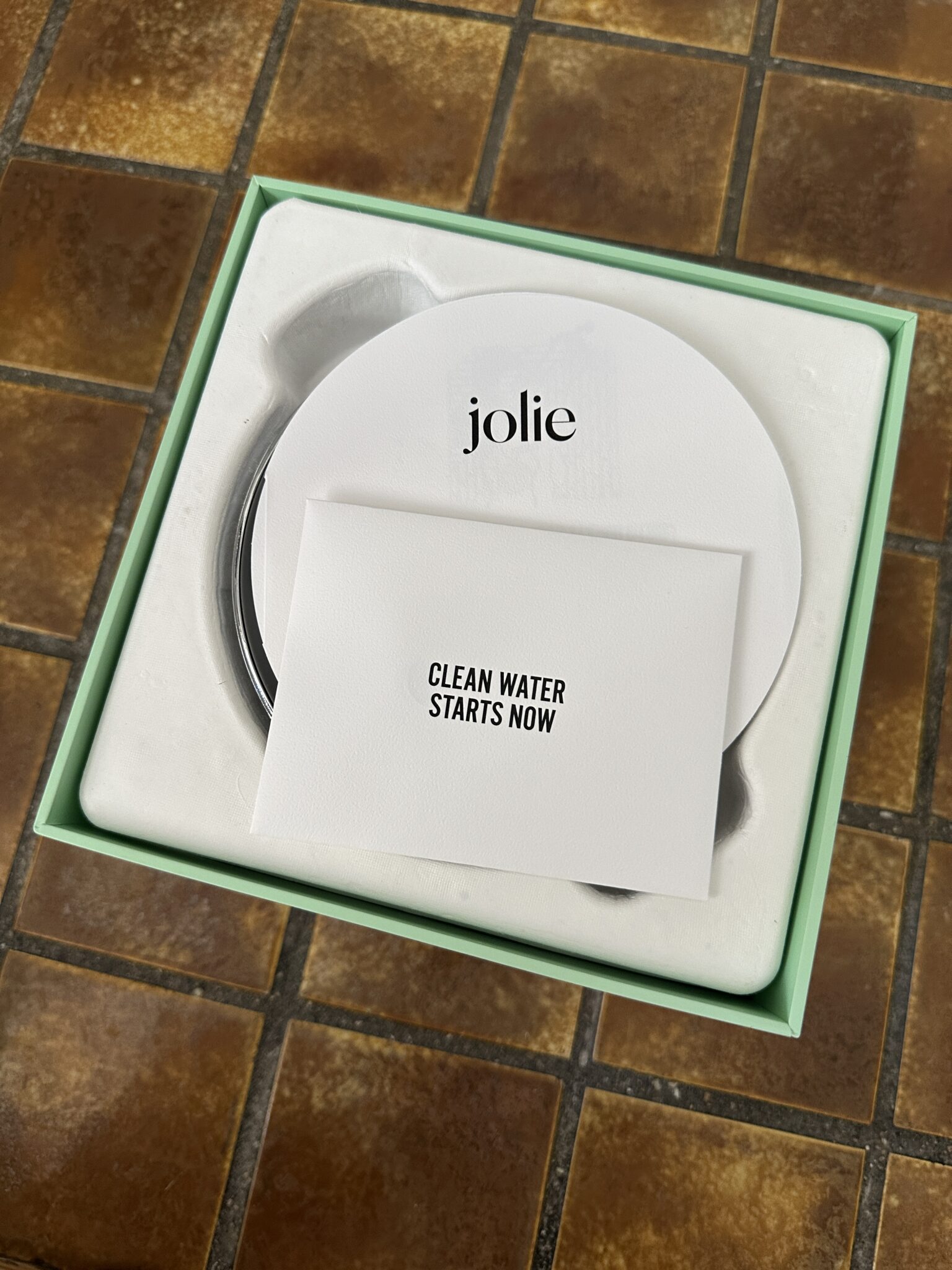 A boxed Jolie product with a card on top that reads "CLEAN WATER STARTS NOW," placed on a brown tiled surface.