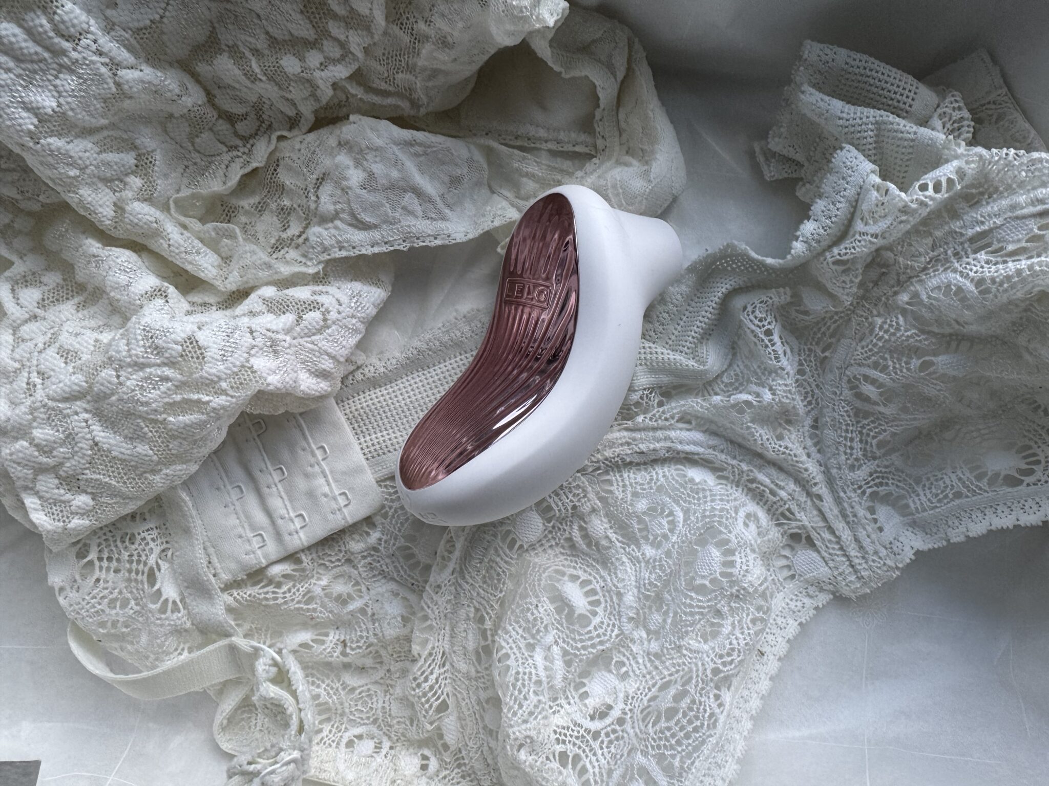 A small white and rose-colored personal massager rests on top of white lace lingerie.