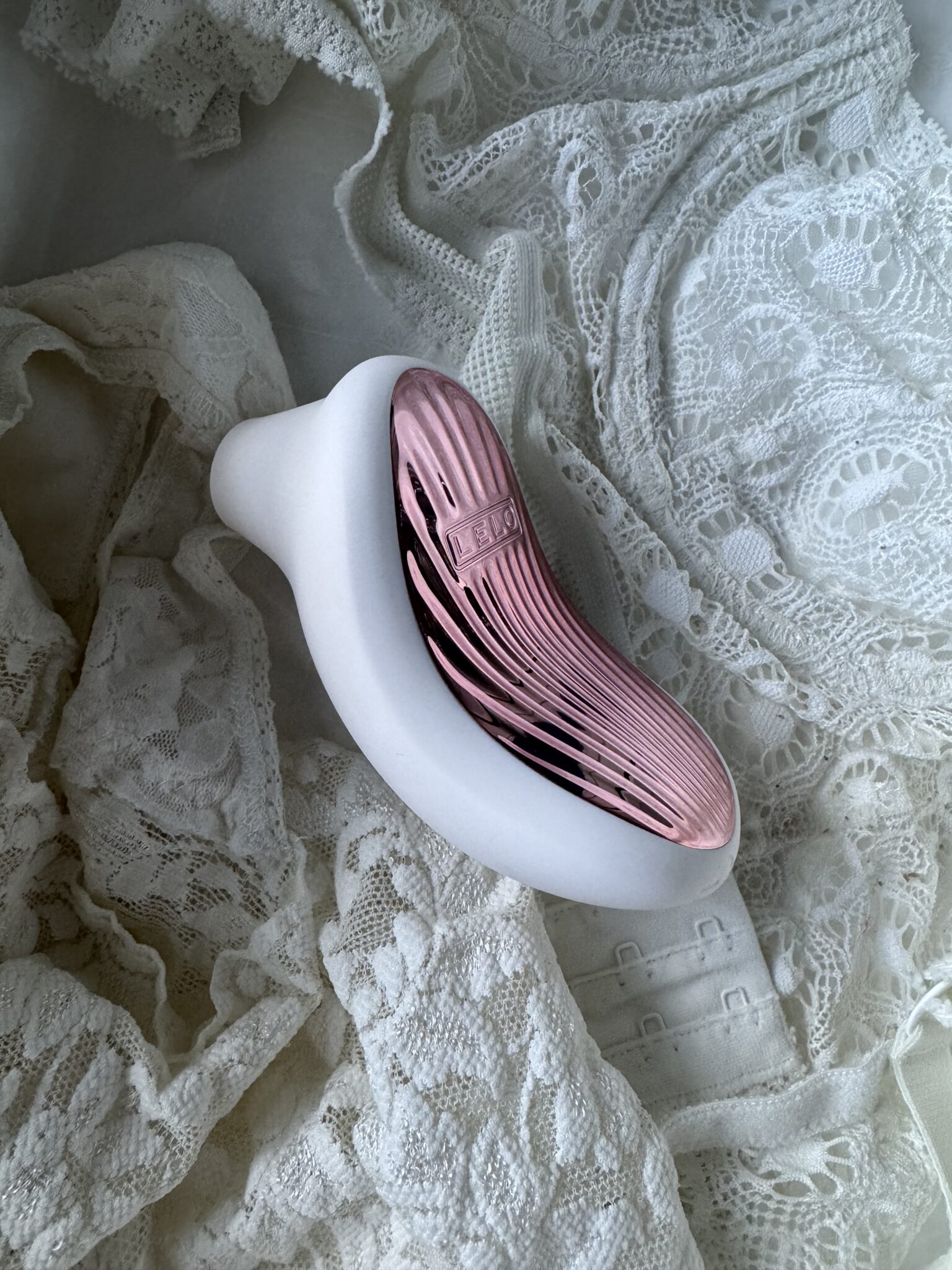 A modern, curved white and pink device rests on intricately patterned white lace fabric.