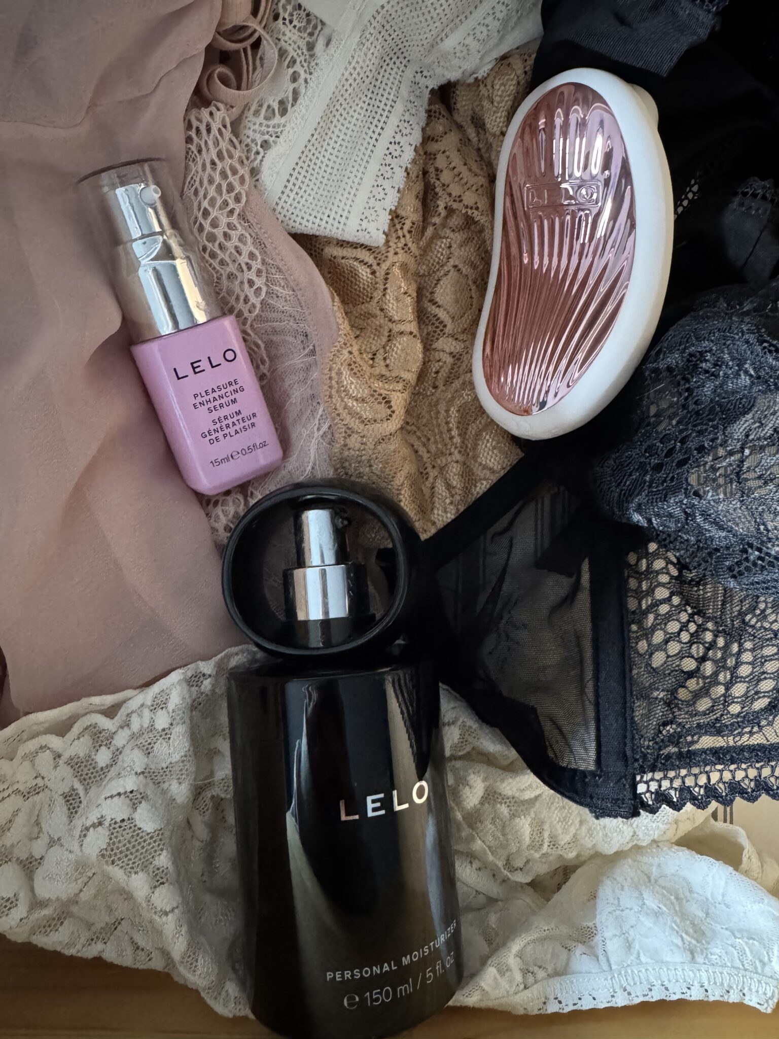 A bottle of LELO personal moisturizer, a tube of LELO cleaner spray, a LELO-branded device, and various lace lingerie pieces laid out in a drawer.