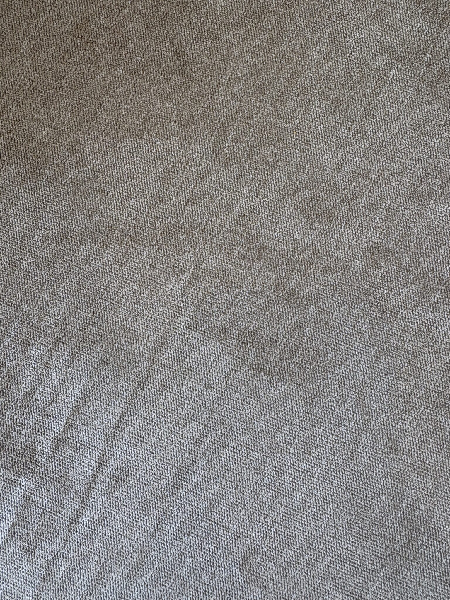 A close-up of beige textured fabric with visible weave patterns and subtle creases.