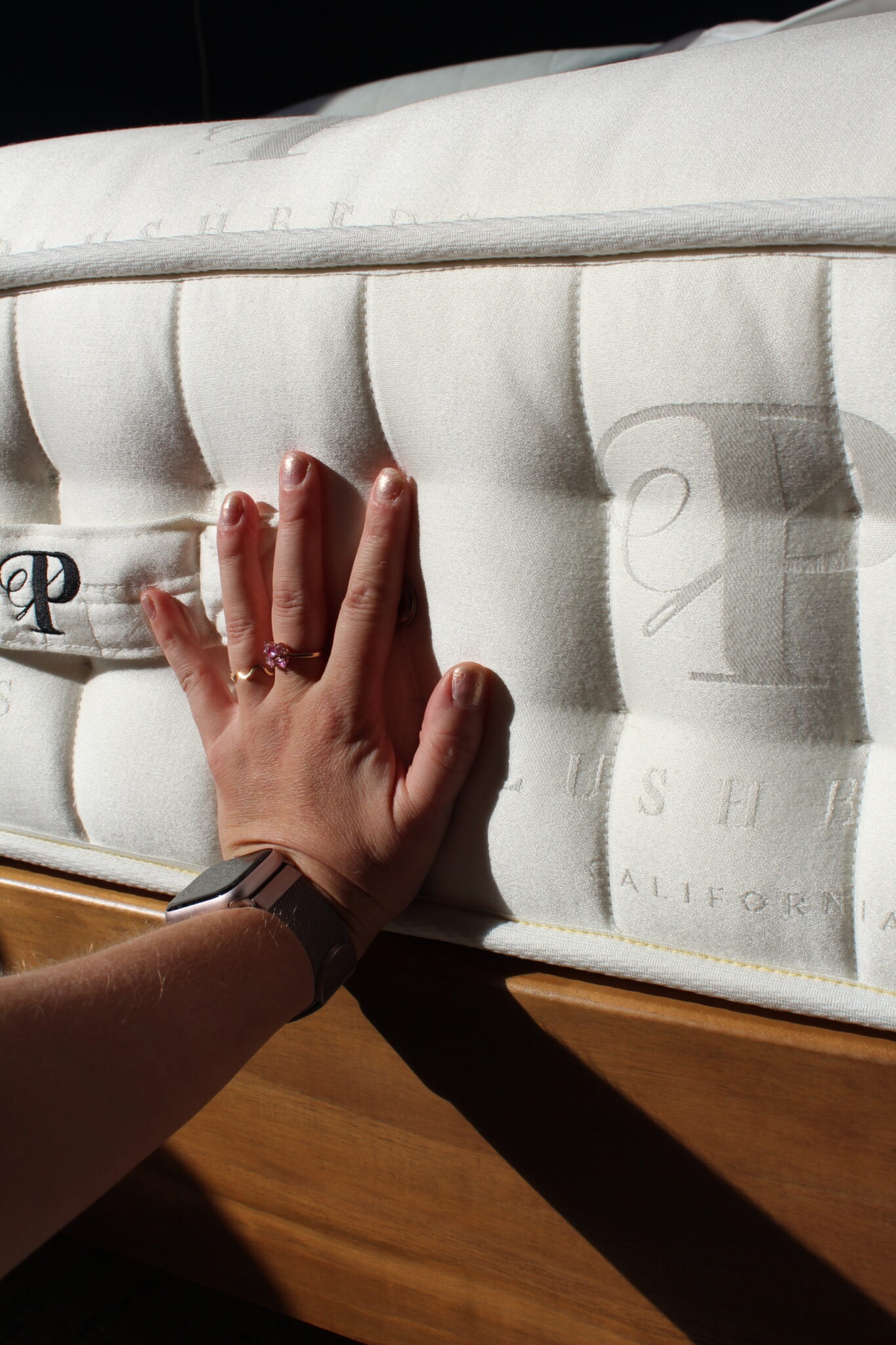 A person presses their hand against a white, tufted mattress with embroidered text, showing the mattress's firmness.