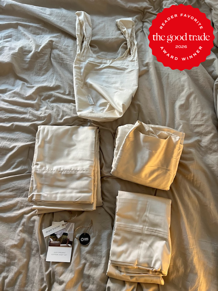Folded cream-colored bedding sets and a reusable bag are arranged on a bed, with product tags and a keychain nearby. A “Reader Favorite: The Good Trade 2026 Award Winner” badge is present.