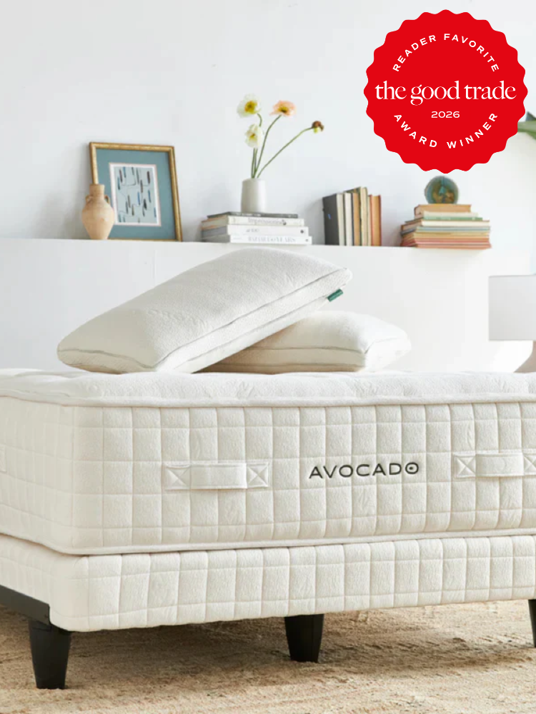 A neatly made Avocado mattress with pillows is shown in a bright, minimalist bedroom. A "Reader Favorite" award badge from The Good Trade is displayed in the top right corner.