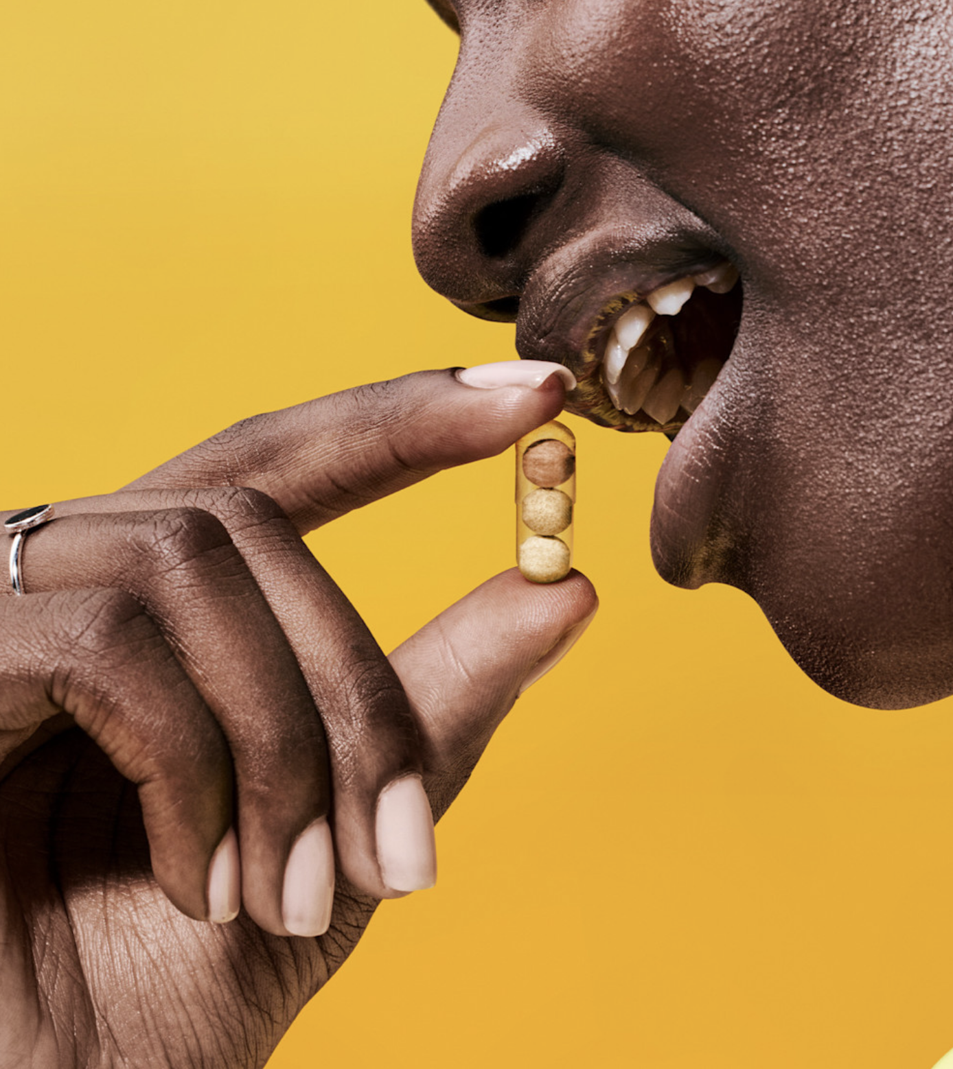A person holds a yellow capsule between their fingers, about to place it in their mouth, with a yellow background.